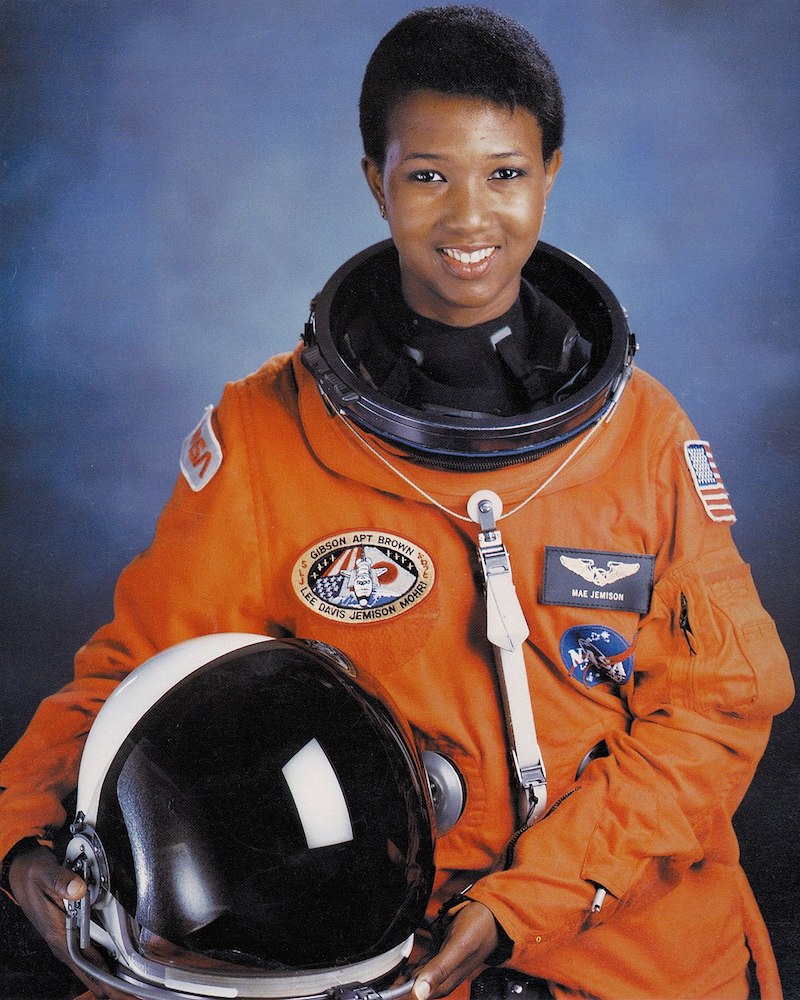 Mae Carol Jemison in an orange space suit holding their helmet to their side