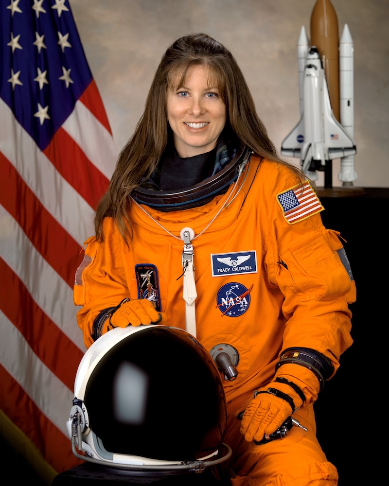Tracy Caldwell in an orange space suit with their helment in front of them